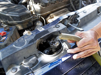 Cropped hand pouring water in vehicle engine through pipe