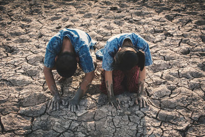 High angle view of siblings kneeling on barren landscape