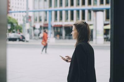 Side view of woman standing against text in city