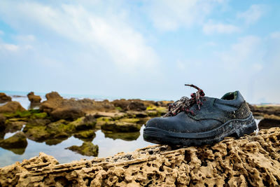 Close-up of shoes on rock by sea against sky