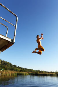 Low angle view of man jumping against clear blue sky