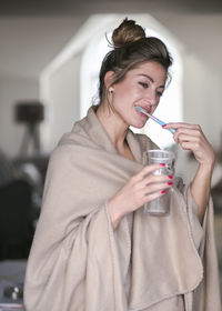 Young woman brushing teeth while holding glass of water