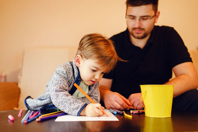 Father looking at son making drawing on table at home