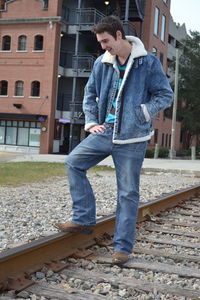 Young man standing on railroad track against buildings in city