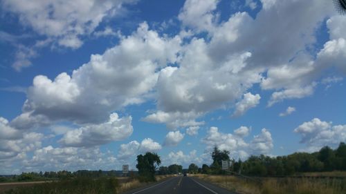 Road passing through field against cloudy sky