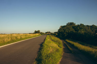 Road amidst field against clear sky