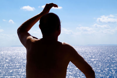 Rear view of shirtless man looking at sea on sunny day