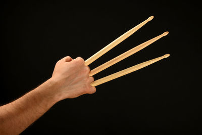 Cropped hand holding drumsticks against black background