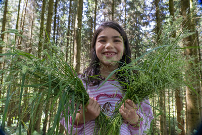 Portrait of smiling girl in forest with bushes in hand