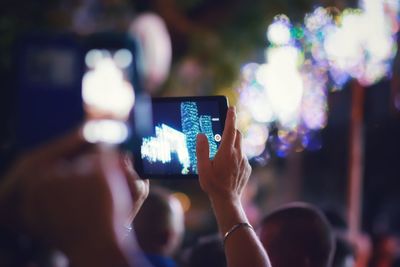 Cropped hands photographing illuminated lights with digital tablet at night