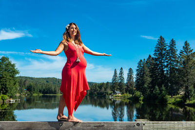 Low angle view of pregnant woman standing against lake