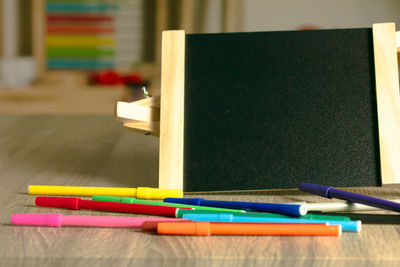 Close-up of colorful felt tip pens with blackboard on wooden table