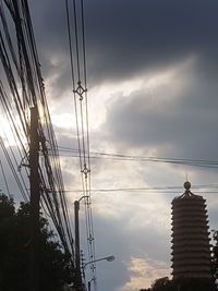 Low angle view of silhouette electricity pylon and building against sky