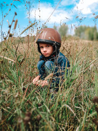 A small boy in a motorcycle helmet is hiding in the grass and glowering