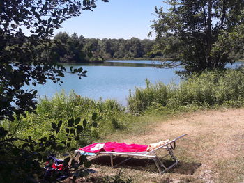 Chairs by lake against clear sky