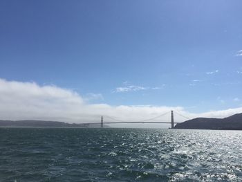 Scenic view of suspension bridge over sea against blue sky