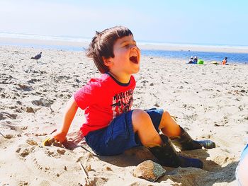 Boy sitting on beach by sea against sky