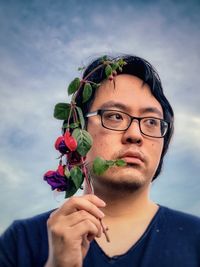 Close-up of young man holding fuchsia flowers against cloudy blue sky.