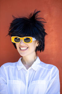 Portrait of young woman wearing sunglasses standing against yellow wall