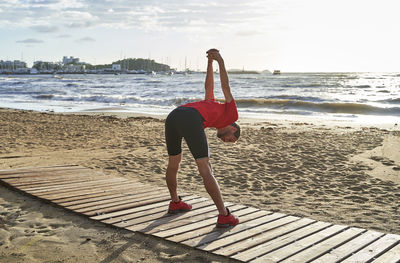 Man stretching hands on boardwalk at beach