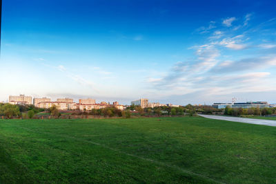 Scenic view of field by buildings against blue sky