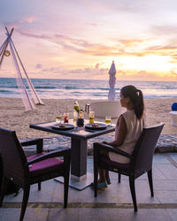 Rear view of woman sitting on table at beach