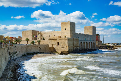 Buildings in sea against cloudy sky