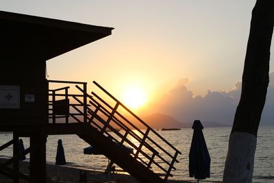 Silhouette railing by sea against sky during sunset