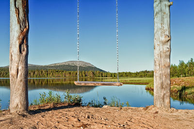 A wooden swing hangs by the still water of a beautiful lake at the finnish lapland. 