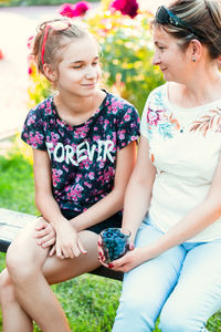 Smiling mature woman with blueberries looking at daughter sitting on bench