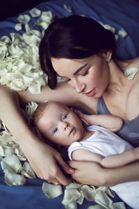 Mother brunette with a newborn boy lies on the bed with white rose petals
