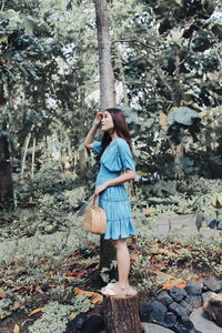 Side view of young woman standing against trees in forest