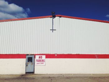 Warning sign board on factory building against sky