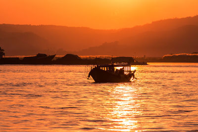 Silhouette boat in sea against orange sky