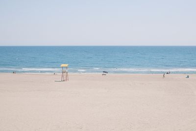 Rear view of woman walking at beach against clear sky
