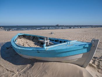 Boat moored on beach against clear blue sky