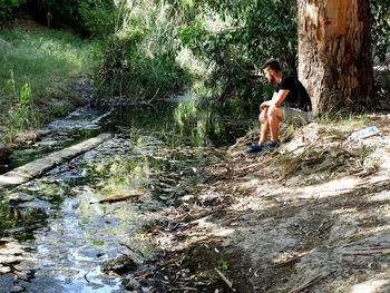 Side view of young woman standing by river in forest