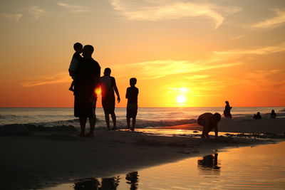 Silhouette people on beach against sky during sunset