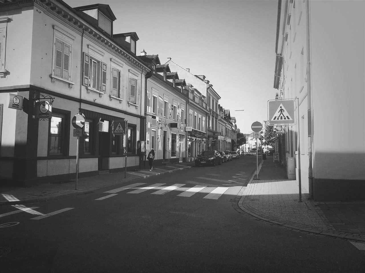 architecture, built structure, building exterior, street, transportation, clear sky, road, city, car, incidental people, sky, the way forward, building, land vehicle, day, street light, outdoors, sunlight, mode of transport, empty