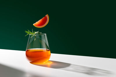 Shiny glass of fresh negroni cocktail with orange slice garnished with sprig of rosemary. 