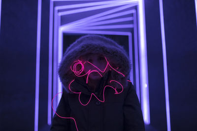 Woman in hooded clothing with light painting standing against illuminated lights