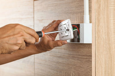 Electrician is using a screwdriver to install a power outlet in to a plastic box on a wooden wall.