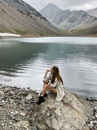 Woman sitting by lake against mountains