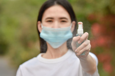 Portrait of young woman wearing mask holding hand sanitizer outdoors