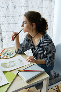 Millennial girl draws fabulous images on paper while sitting at home