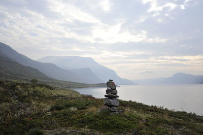 Stack of rocks on grassy mountains by sea against cloudy sky at jotunheimen national park