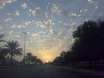 Road by silhouette trees against sky during sunset
