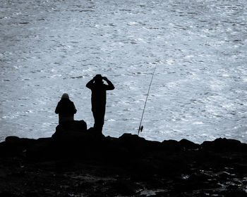 Silhouette man and woman standing on rock by sea