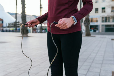 Crop faceless female in sportswear and fitness tracker preparing for exercising with skipping rope during outdoor workout on city square