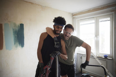 Smiling male homosexual couple standing together during apartment renovation